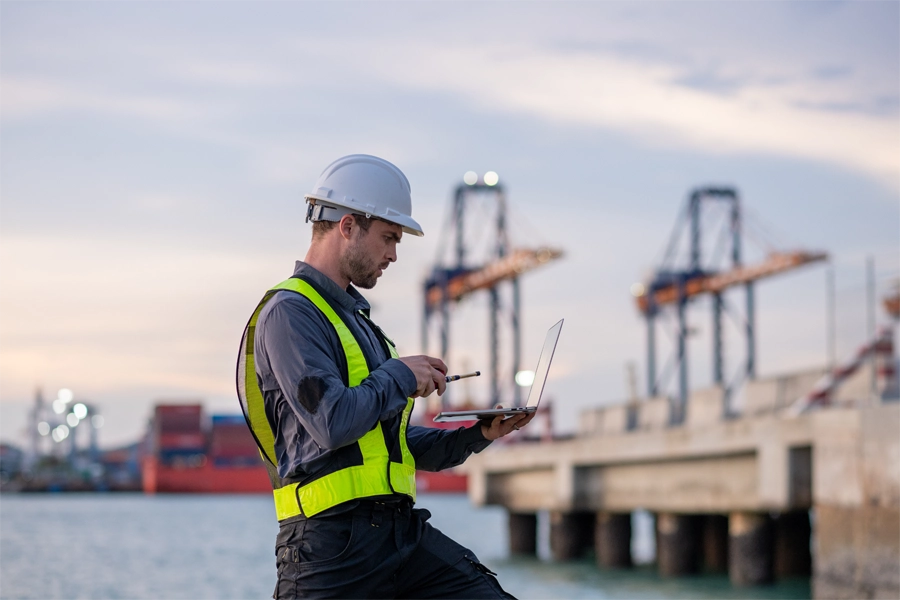 Imagem: técnico em comércio exterior utiliza um notebook para controlar chegada e saída de mercadorias em porto.