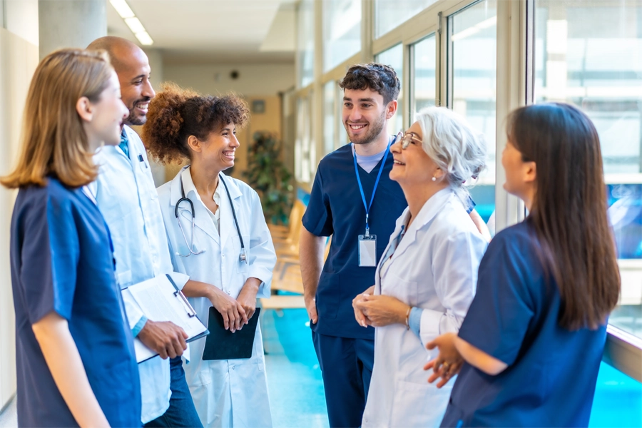 Imagem: equipe de técnicos em enfermagem, médicos e enfermeiros conversam em corredor de hospital.