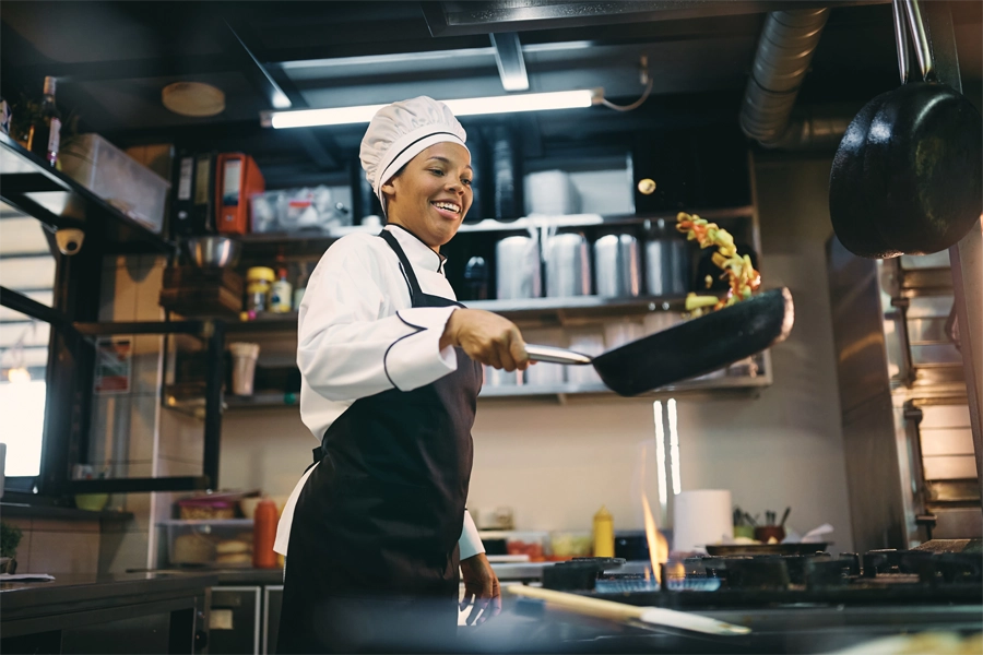Imagem: chef de cozinha sorri enquanto faz um preparo na frigideira.