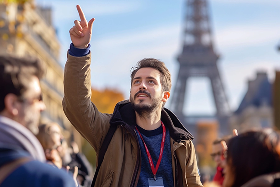 Grupo de pessoas reunido ao ar livre com a Torre Eiffel ao fundo. Um guia de turismo ao centro levanta a mão apontando para cima. Os rostos estão desfocados por privacidade. Céu claro e folhagem outonal visível nas árvores.