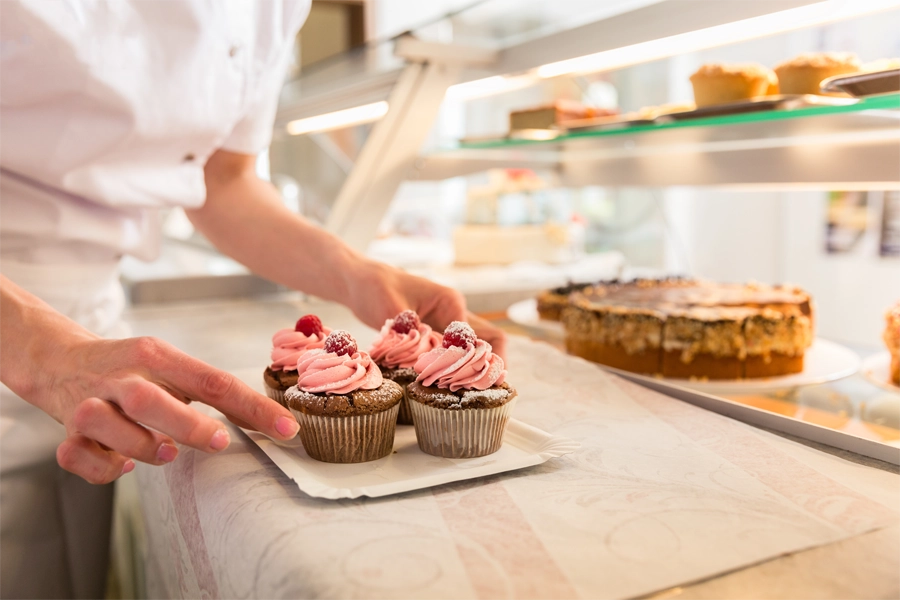 Imagem: uma confeiteira faz os ajustes finais em um cupcake com cobertura rosa.