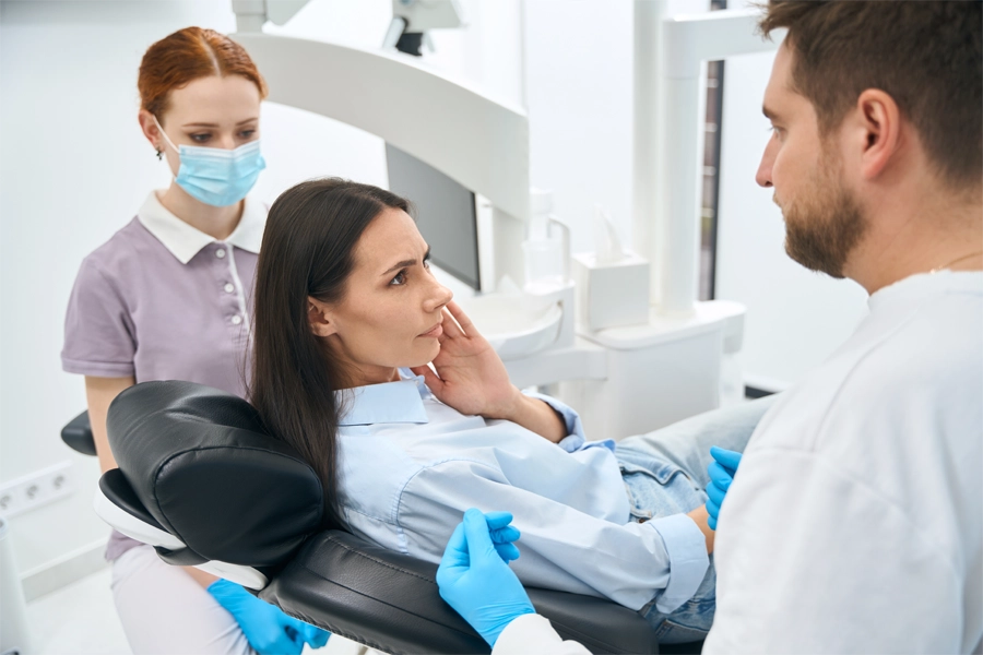 Imagem: uma paciente apoia a bochecha com a mão indicando ao dentista e ao técnico em saúde bucal onde está doendo.