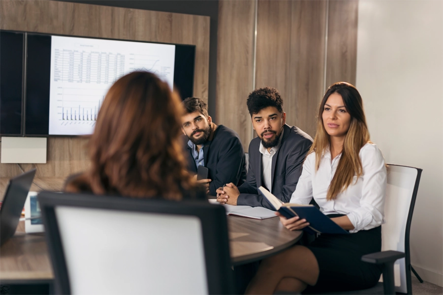 Imagem: três profissionais de gestão em recursos humanos entrevistam uma candidata em sala de reuniões corporativas de uma empresa.