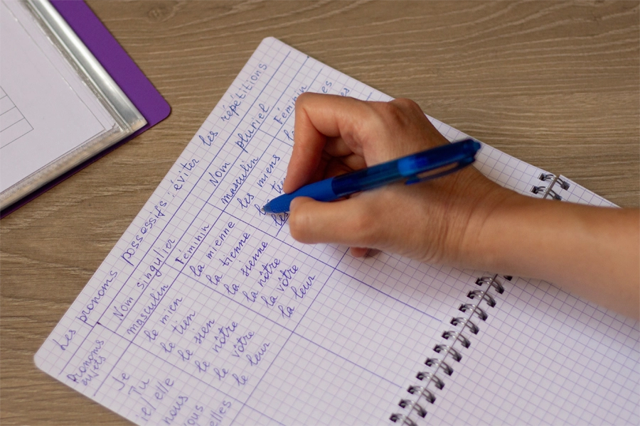 Imagem:  a mão de um estudante anota a gramática de francês em um caderno. Foto em close-up.
