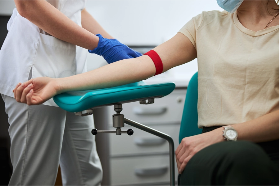 Imagem: técnico em análises clínicas prepara o braço de paciente para coletar sangue.