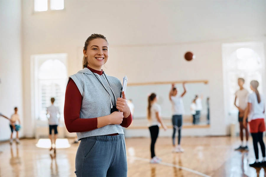 Professora de educação física dando aula de vôlei para uma turma de estudantes em uma quadra esportiva de escola.