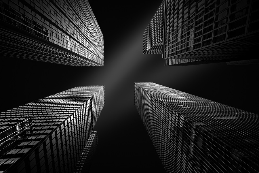 Quatro prédios visto do ângulo de baixo pra cima em fotografia preto e branco.