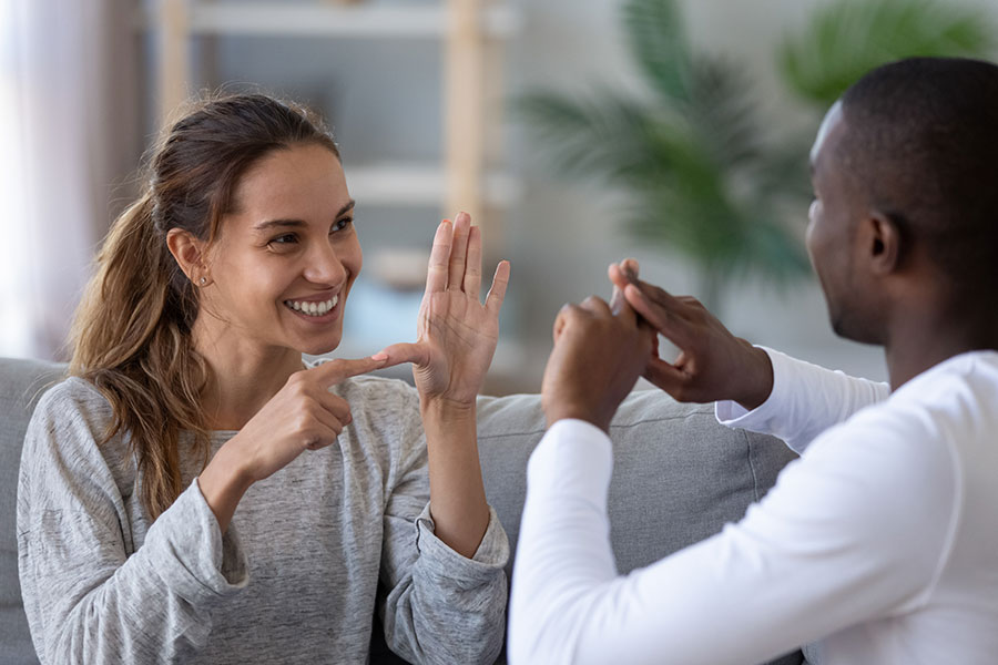 Mulher branca sorrindo conversando em libras de frente para um homem negro