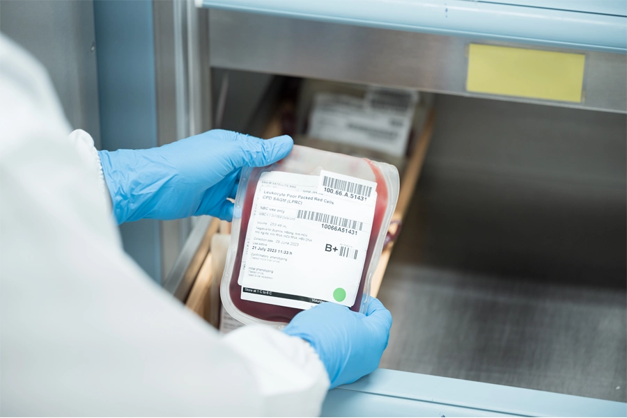 Imagem: técnico em hemoterapia analisa o rótulo de uma bolsa de sangue tipo B+ no laboratório.