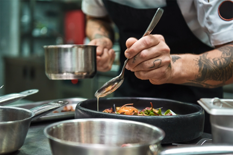 Imagem: close da mão de um chef de cozinha finalizando um prato com molho.