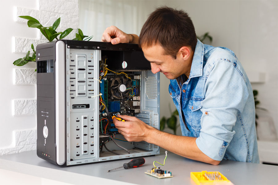 Homem faz a manutenção de sistemas de uma CPU de computador utilizando uma chave especial apoiado numa mesa.