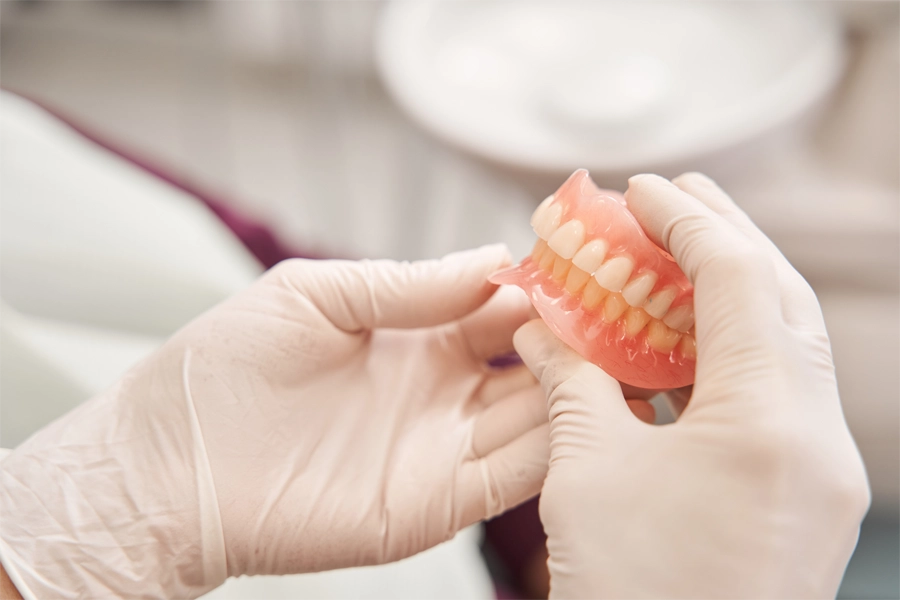 Prótese dentária completa sendo segurada por profissional com luvas, em ambiente clínico odontológico. Ideal para tratamentos de reabilitação oral e prótese dentária.