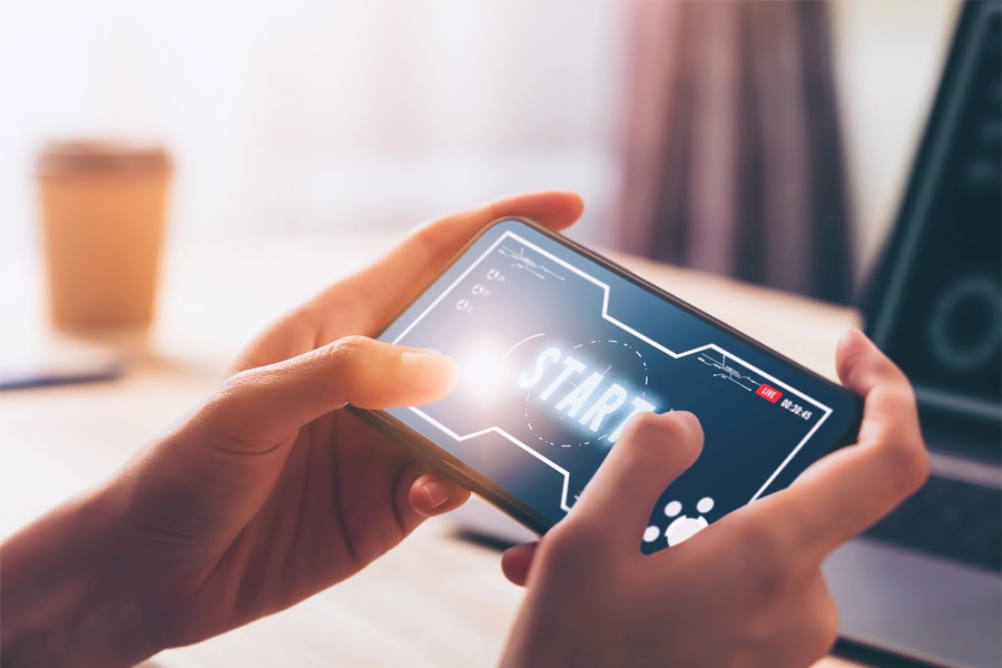 Imagem: close das mãos de um técnico em jogos digitais testando um jogo em smartphone.