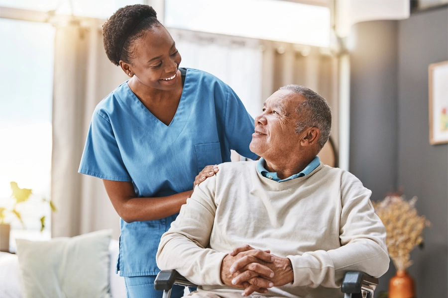 Imagem: enfermeira sorri enquanto olha para paciente de quem cuida, que retribui o olhar e sorri também.