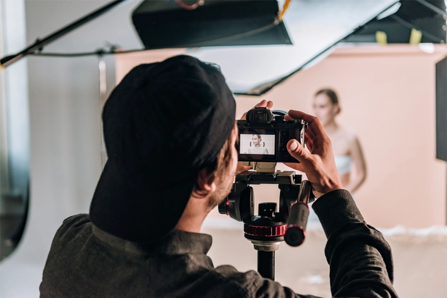 Imagem: fotógrafo em estúdio fotográfico ajustando o enquadramento de uma câmera posicionada para uma modelo.