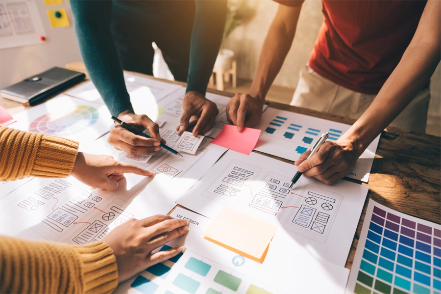 Imagem: mesa com papéis e post-its organizados enquanto designers trabalham no projeto.