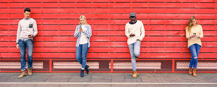 Pessoas encostadas em uma parede vermelha. todos com celulares nas mãos Pessoas encostadas em uma parede vermelha. todos com celulares nas mãos