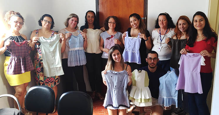 Alunos do curso Costureiro seguram vestidinhos produzidos durante projeto Alunos do curso Costureiro seguram vestidinhos produzidos durante projeto