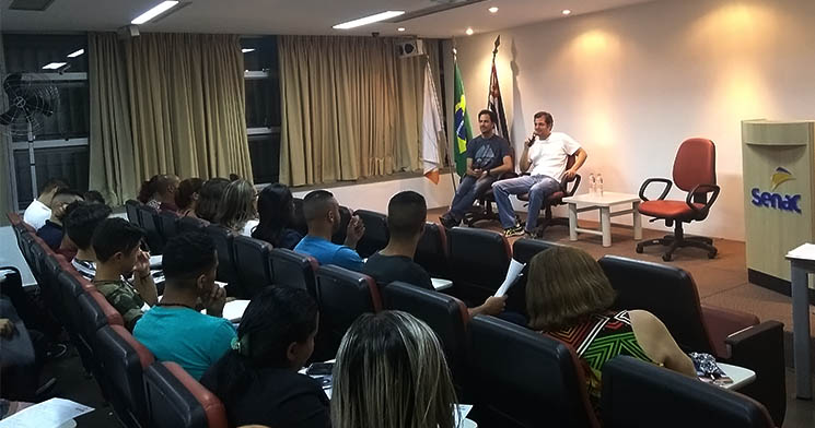 Dois homens sentados em palco falam para plateia Dois homens sentados em palco falam para plateia