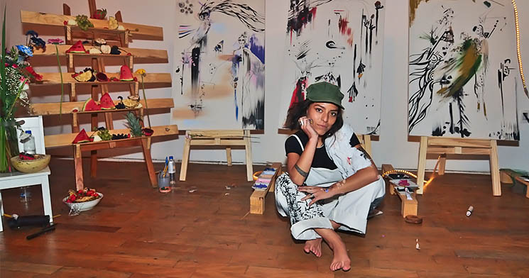 Artista sentada no chão com perna cruzada em frente a tela Artista sentada no chão com perna cruzada em frente a tela