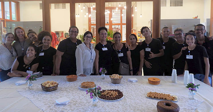Turma reunida lado a lado atrás de mesa com doces e salgados Turma reunida lado a lado atrás de mesa com doces e salgados