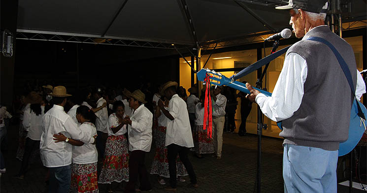 Idoso canta de toca instrumento em palco enquanto casais dançam Idoso canta de toca instrumento em palco enquanto casais dançam