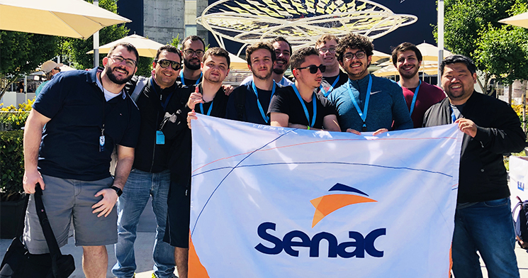 Alunos do Centro Universitário Senac seguram bandeira com logomarca do Senac em conferência da Apple Alunos do Centro Universitário Senac seguram bandeira com logomarca do Senac em conferência da Apple