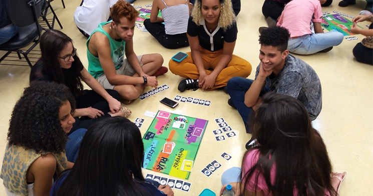 Foto de jovens sentados no chão em círculo e um jogo de tabuleiro ao centro Foto de jovens sentados no chão em círculo e um jogo de tabuleiro ao centro